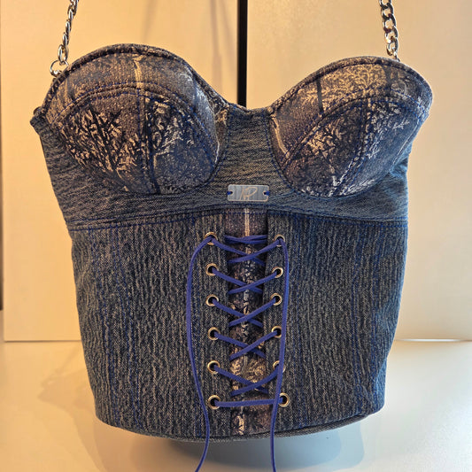A corset-style shoulder bag made from distressed denim, featuring a lace-up front, silver-tone chain straps, and a small mirrored plaque on the front.