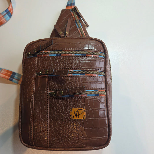 A brown crocodile-embossed sling bag with multiple zippered compartments and a plaid patterned strap, shown on a plain light background.