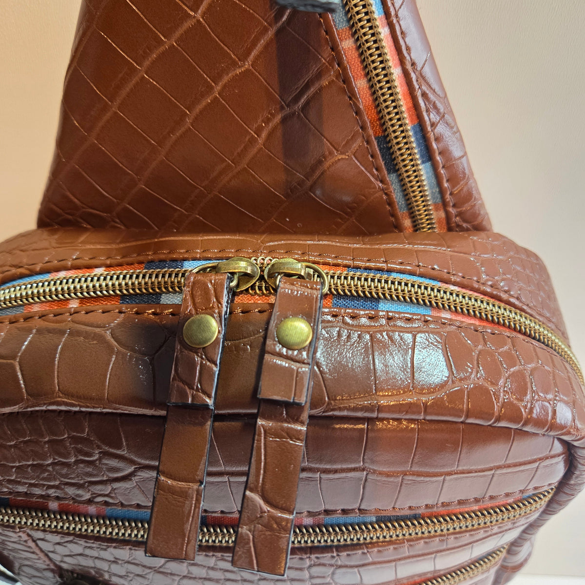 Close-up of a handmade brown textured zippered closure with an embossed crocodile pattern, featuring brass-tone zippers, decorative strap details, and rivets