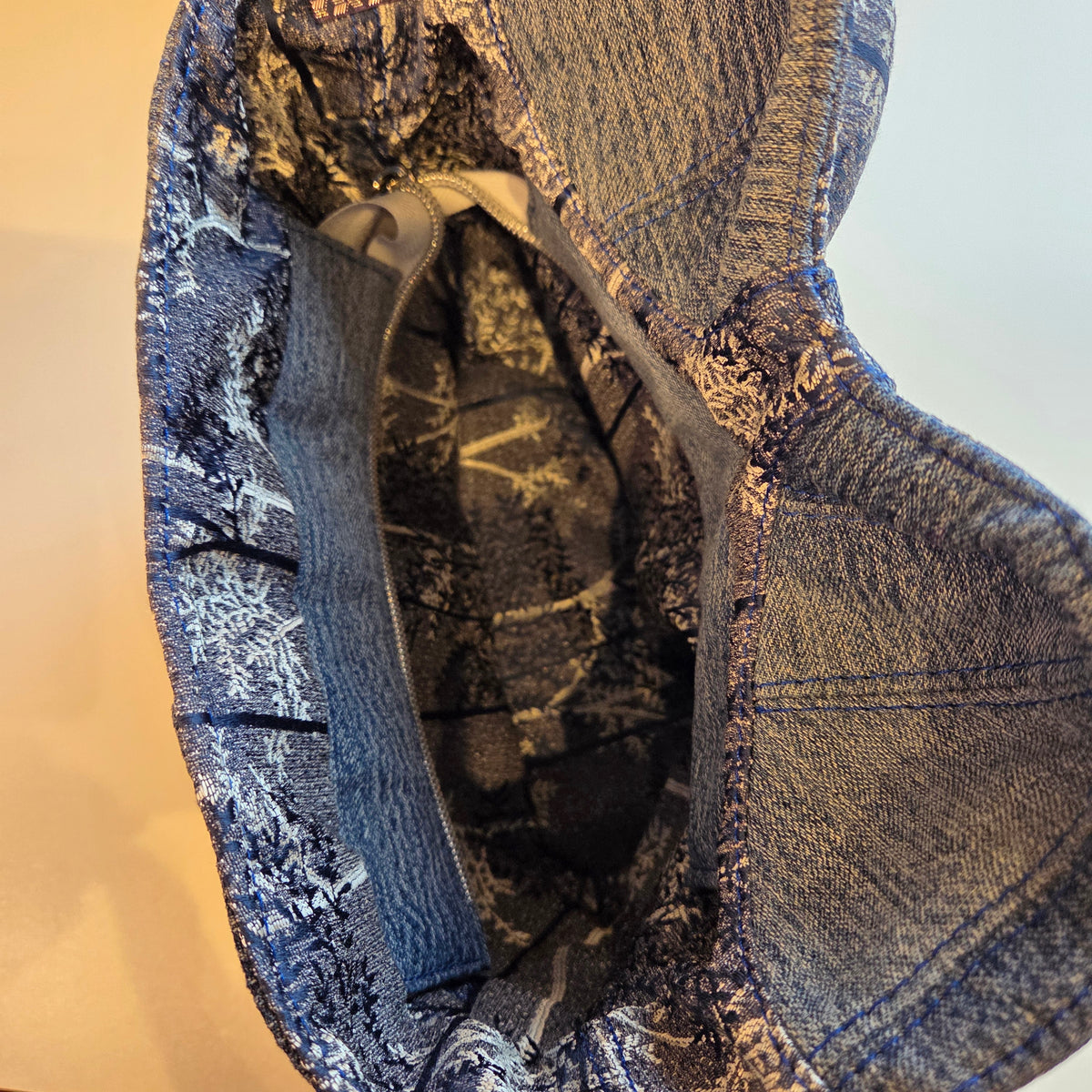 Top view of a denim corset bag with zip open, showing blue lining with dark blue and silver details