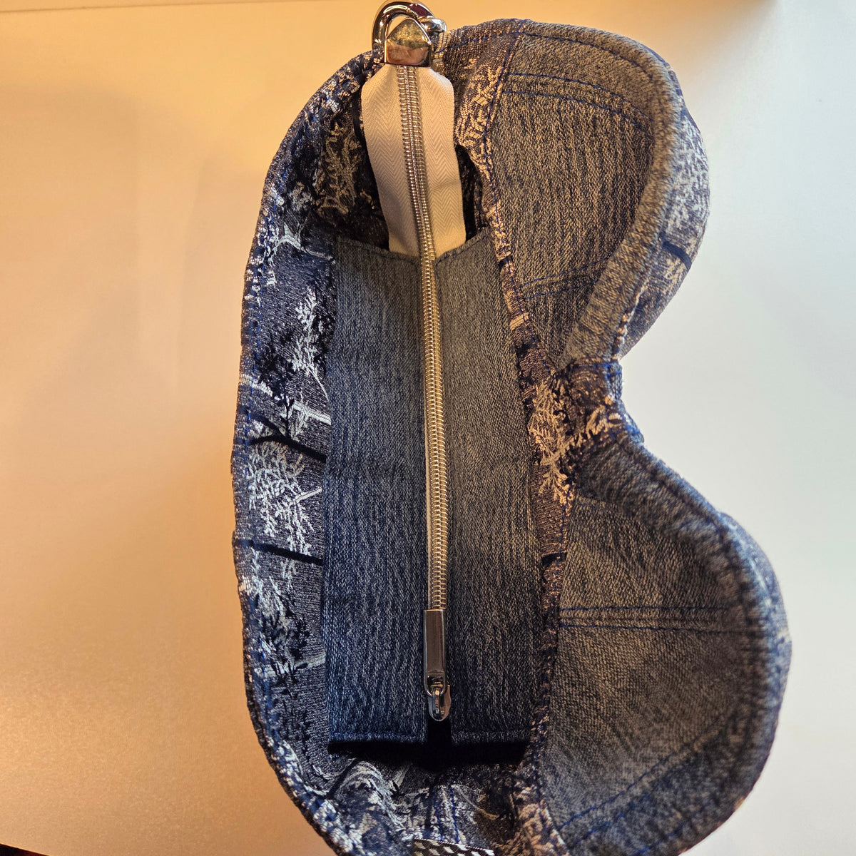 Top view of a denim corset bag with silver tree details and showing zip closure with silver zip teeth and pull