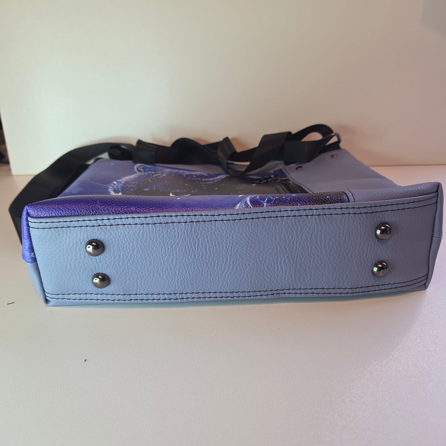 Base of a blue bag showing stitch detail, gun metal bag feet and black strap