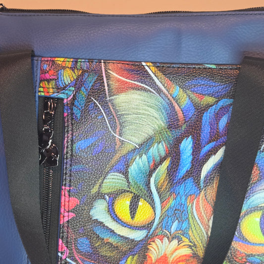 Close-up of a colourful cat design on a blue bag with a cat zipper.