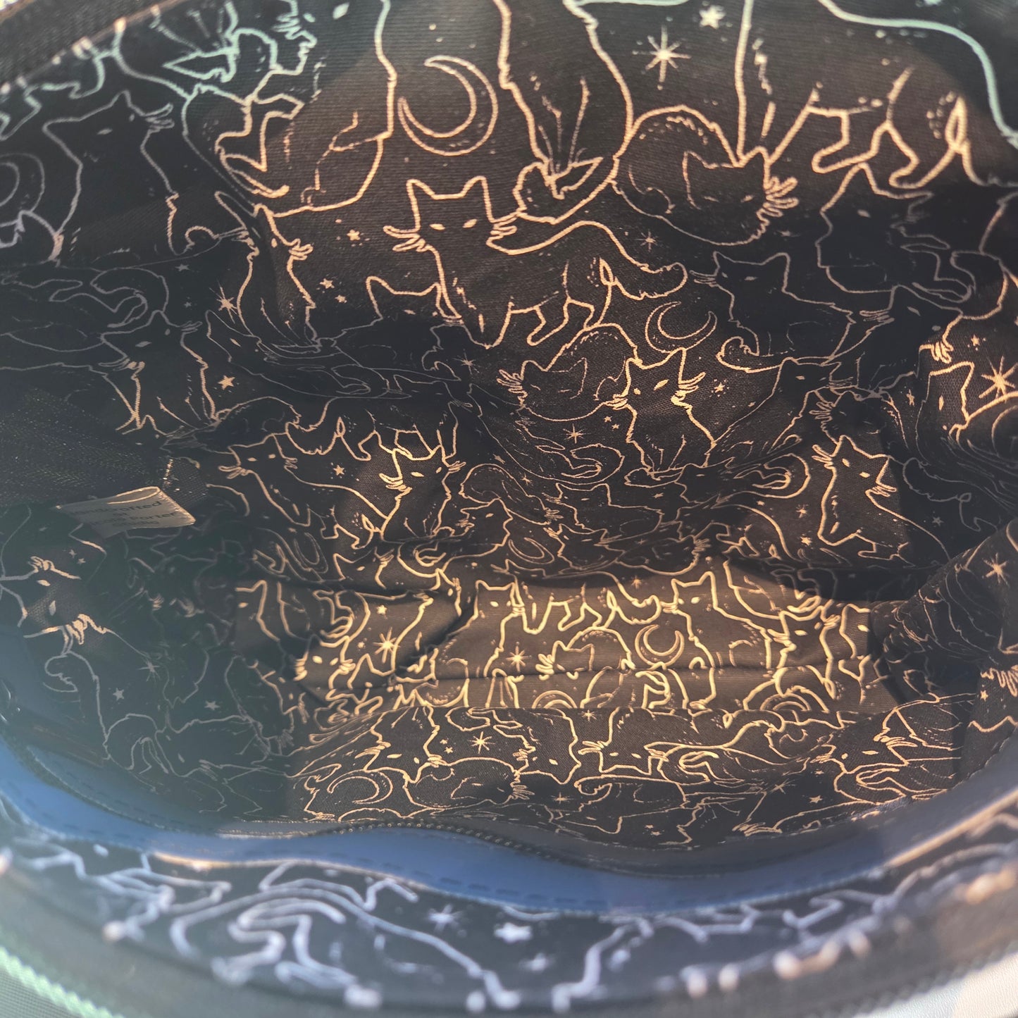 Lining of a bag showing black fabric with white cat outlines and stars