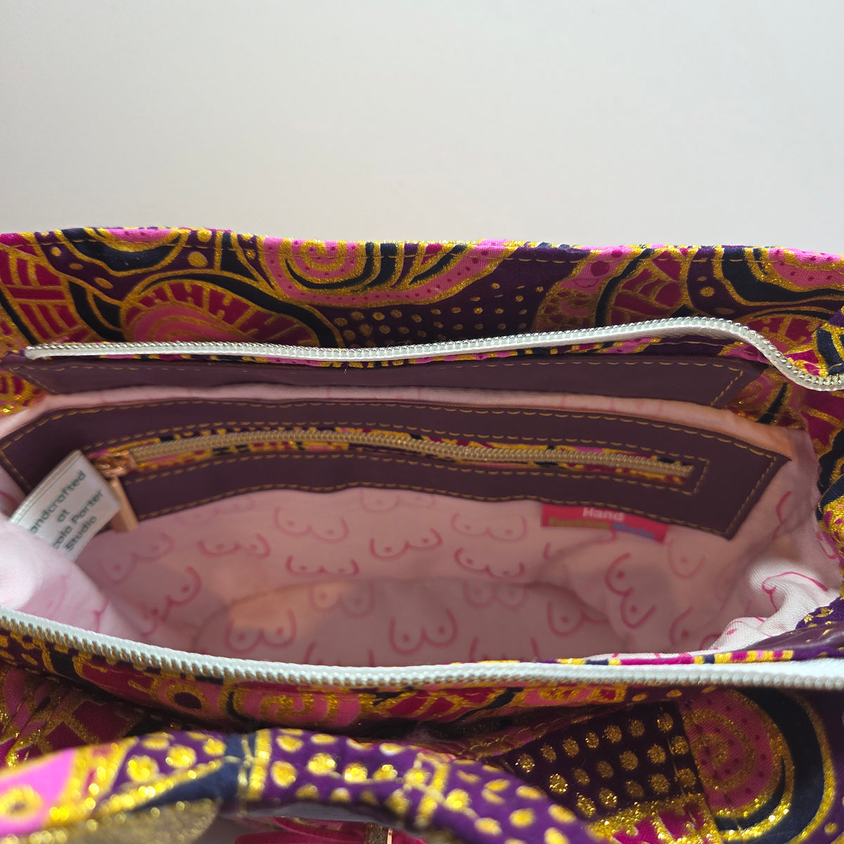 Close-up of a patterned zippered bag interior, showing a purple and pink paisley exterior with a light pink patterned lining and a white zipper.