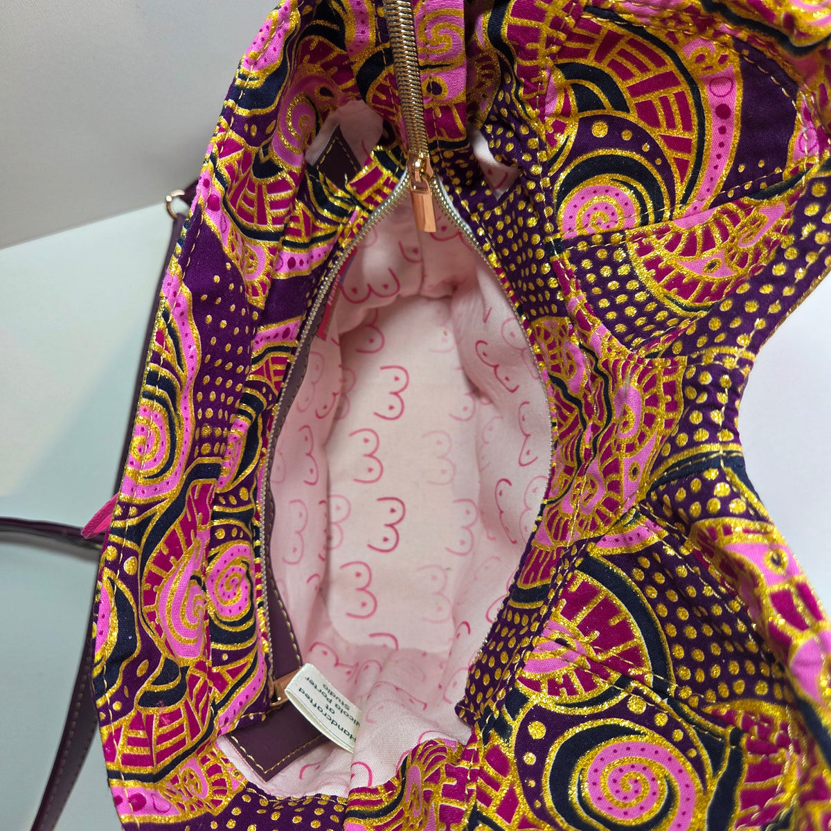 A close-up of a handbag's interior showing a colourful paisley patterned fabric outer and pink lining with cartoon boob prints