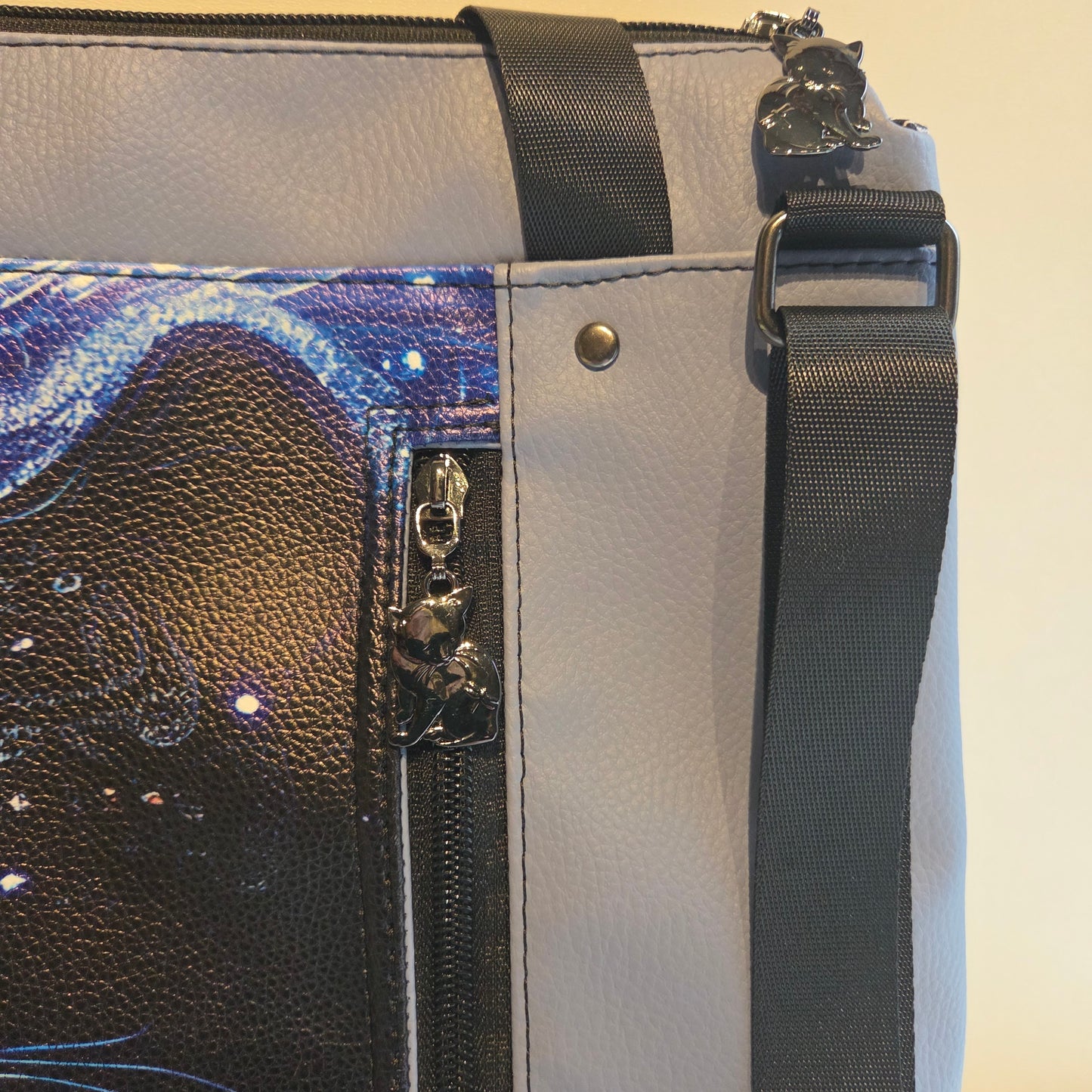 Close-up of a bag with cat zipper pulls and black strap