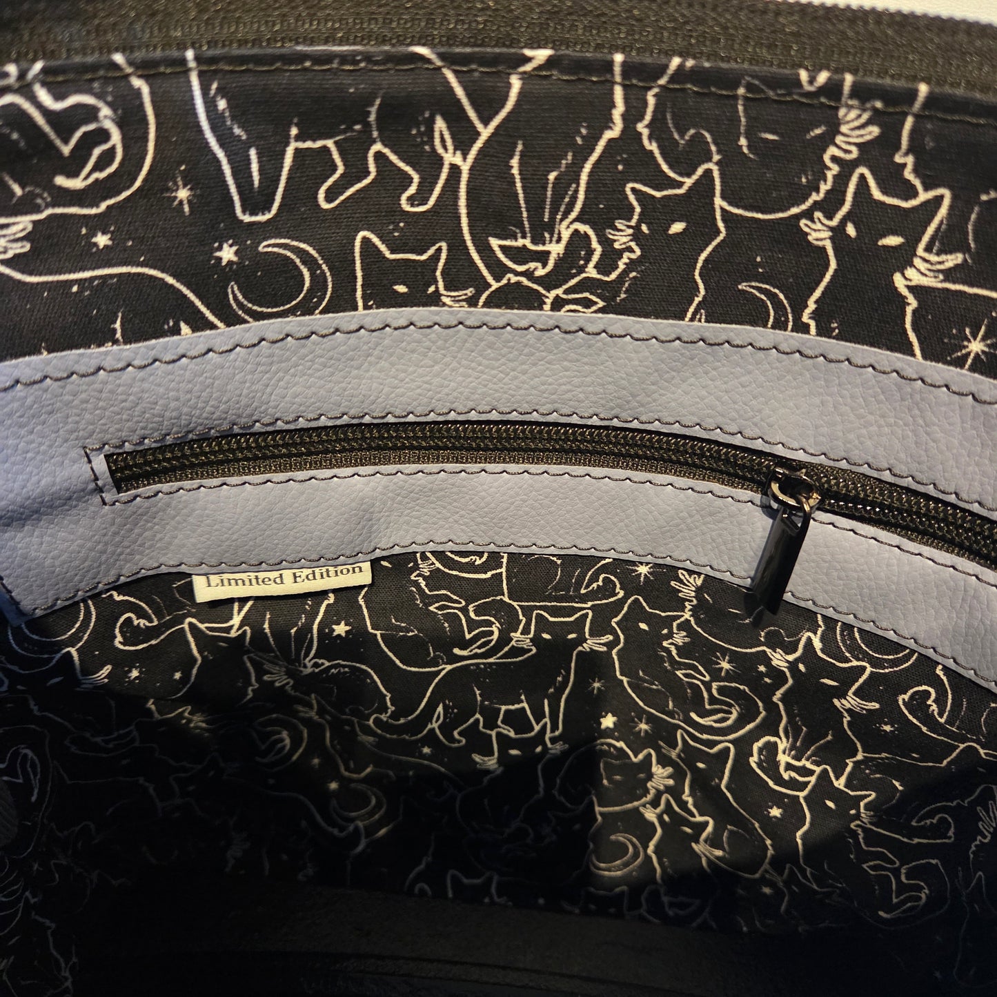 Close-up of a bag lining with zipper pocket and a pattern of cats and stars on a black background.