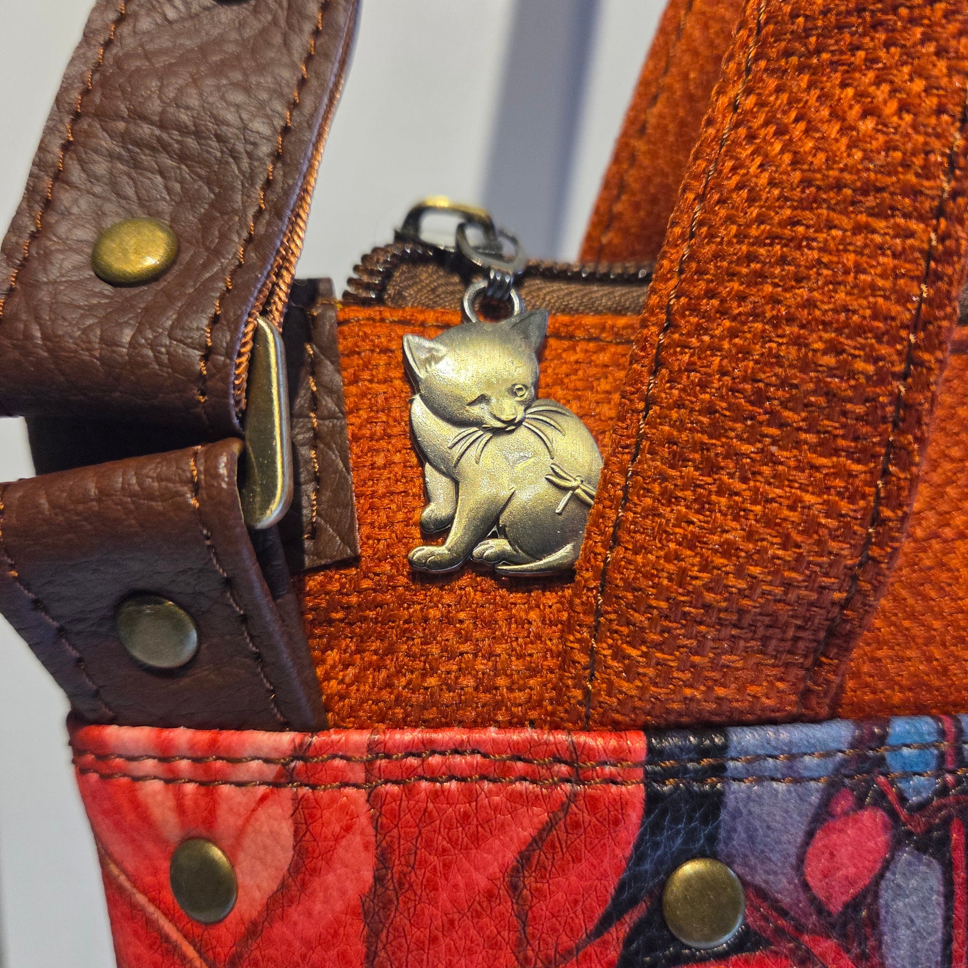 Close up of brass cat zip pull and strap details on an orange bag
