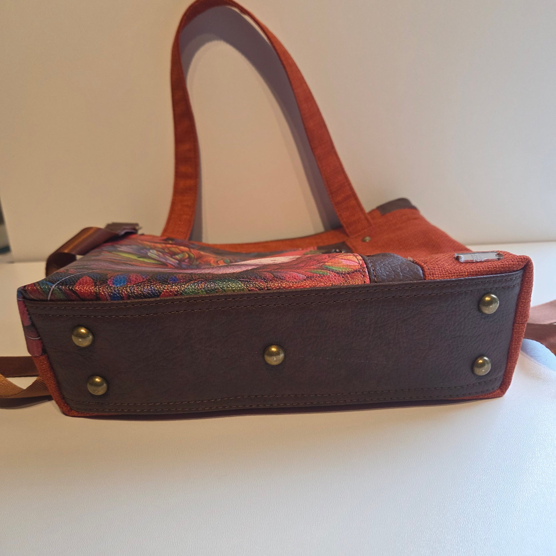 Brown base of an orange bag with brass bag feet.