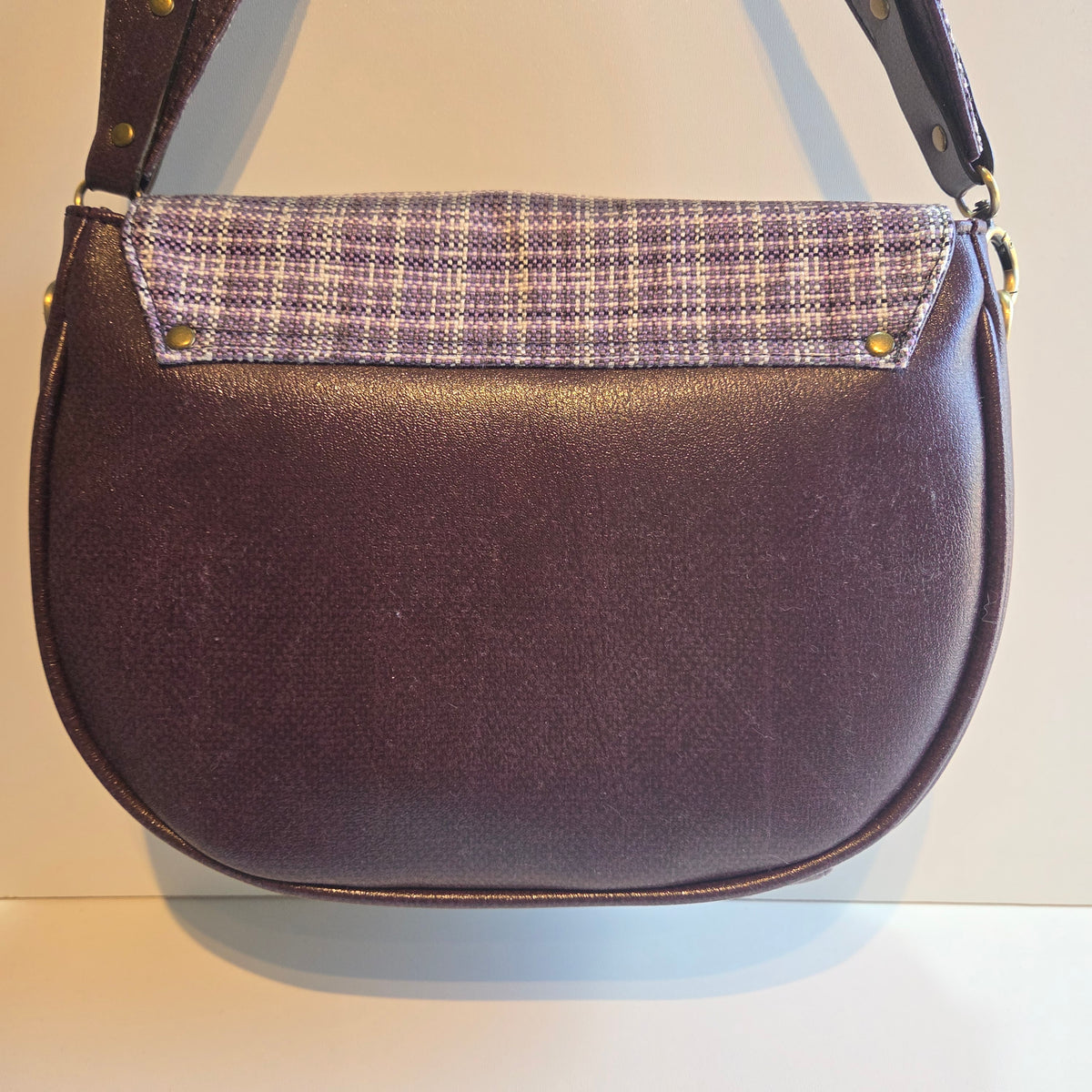 Back view of a purple shoulder bag with a purple and white plaid fabric accent and antique brass hardware