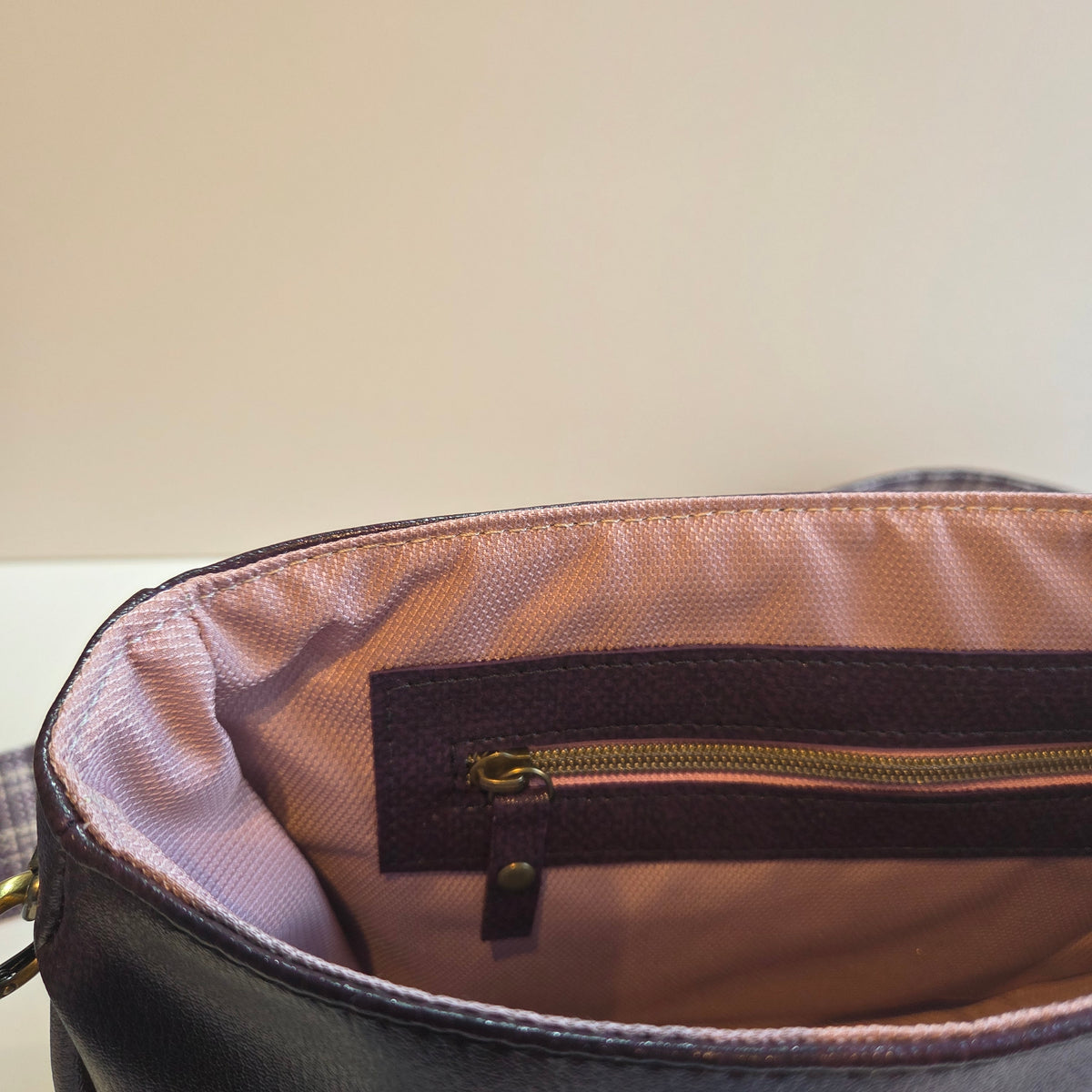 Close-up of the interior of a bag, showing a zippered pocket with a purple zip overlay accent and pink lining, alongside a purple exterior.