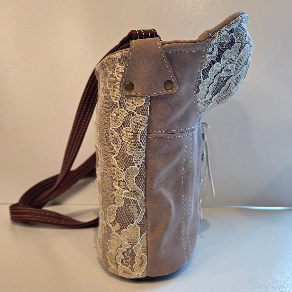 A handmade shoulder bag featuring a dusky pink faux-leather body, a cream floral lace panel, and a maroon strap with cream stitching, set against a plain light background.