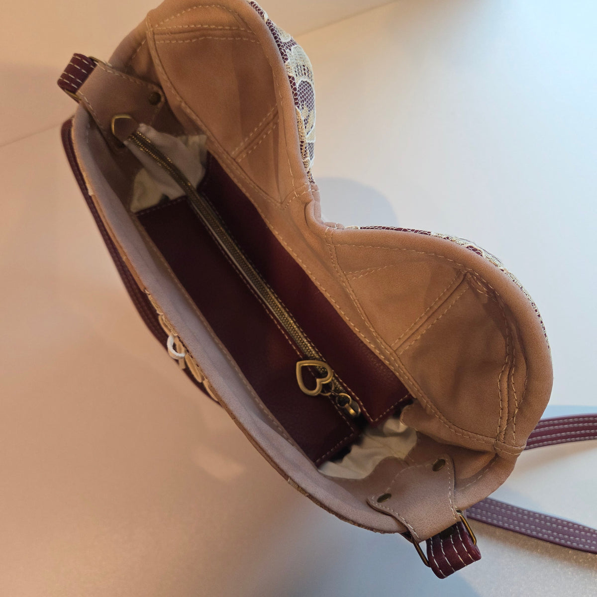 Close-up of the interior of a sculptural shoulder bag made from dusky pink and burgundy fabrics, showing an antique  brass zipper with a heart-shaped pull.